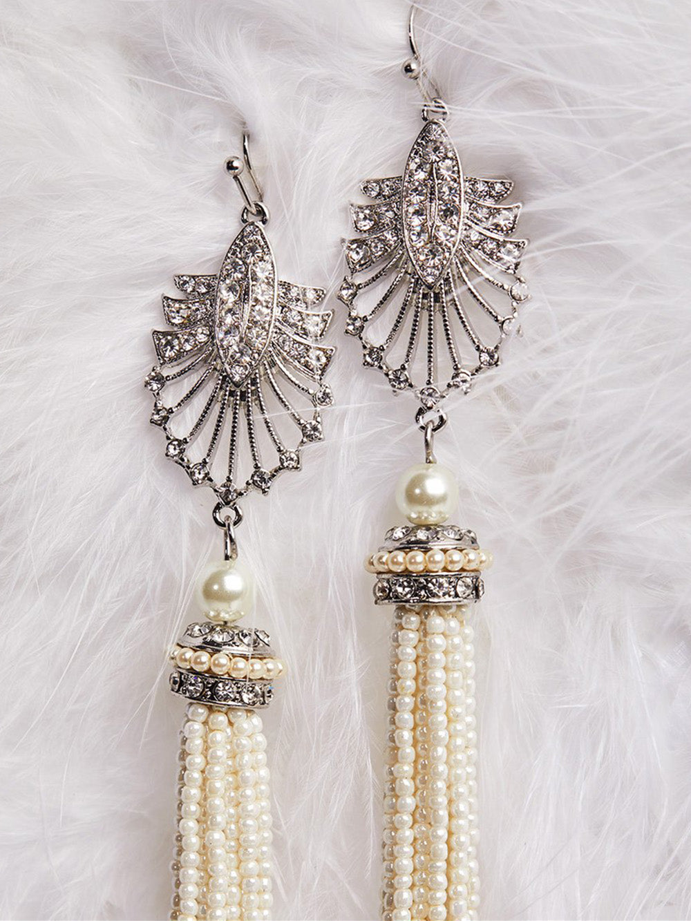 A pair of 1920s Art Deco style pearl tassel earrings displayed on a white fur surface.