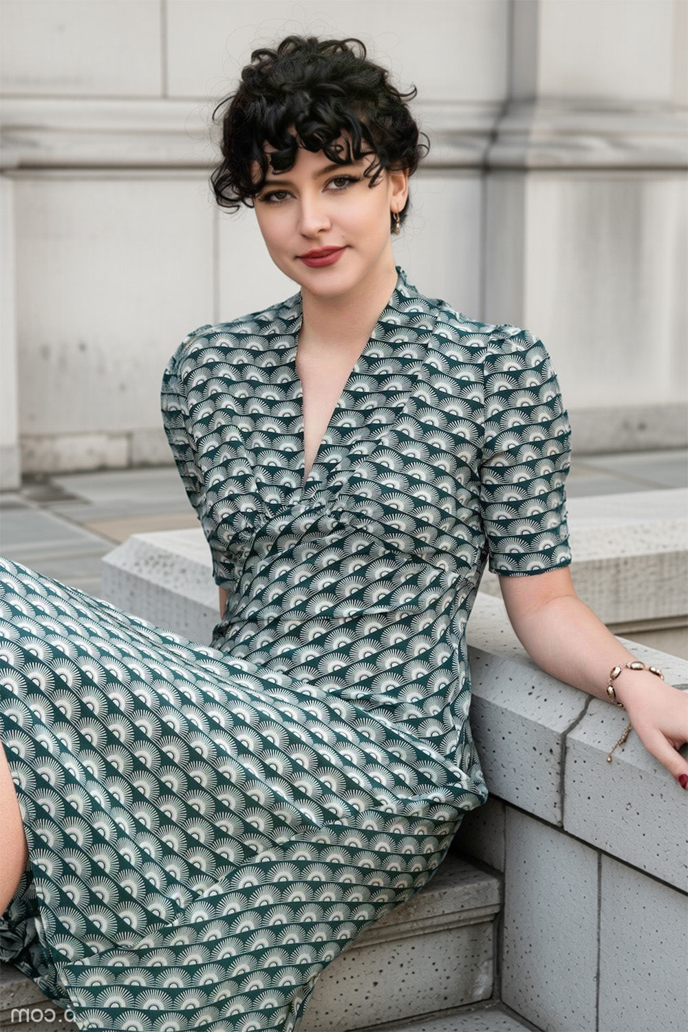 1940s green print dress worn by model sitting on a stone step