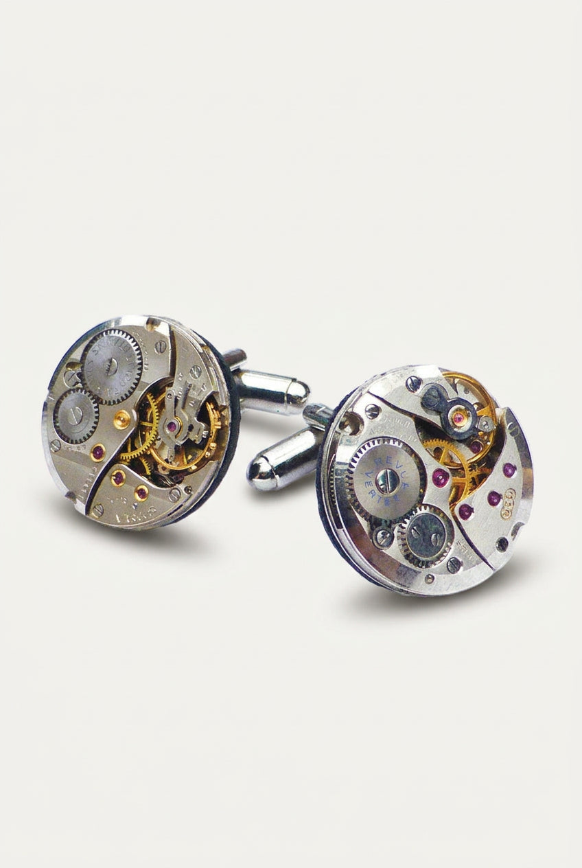 A pair of round cufflinks crafted from vintage-style watch movements, featuring visible gears, bridges, and small colored gemstones on a clean white background.