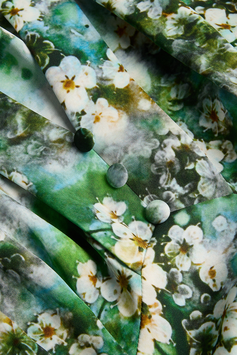 Close-up of a button-front garment with a green and white floral print, showing fabric folds and round buttons.