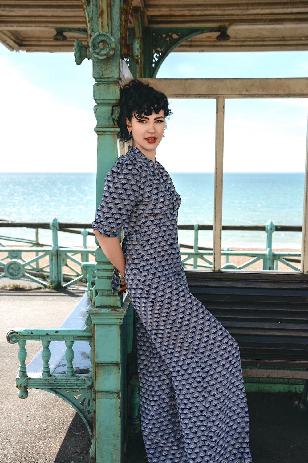 Woman in a navy geometric patterned jumpsuit standing by a bench by the sea